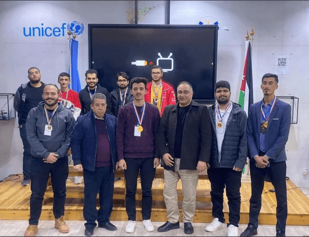 Group of people posing on a stage with medals in front of a UNICEF sign and flags.